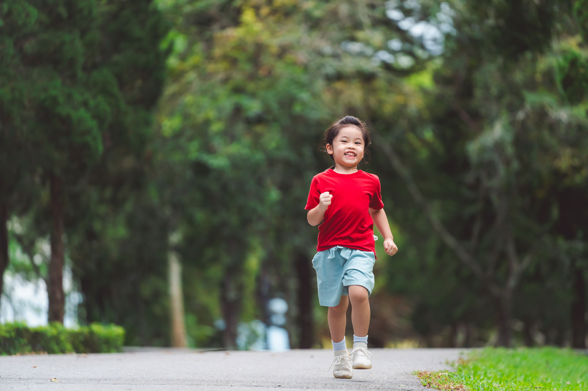 An active Malaysian primary school child running on a park path in everyday shoes